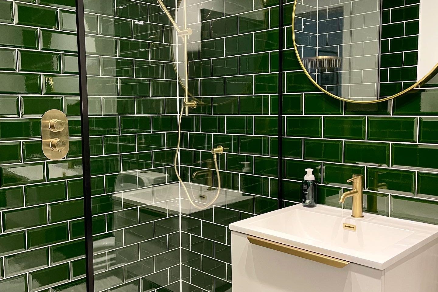New Bathroom, racing green tiles, new shower with gold fittings and a round mirror above an enclosed fitted sink.